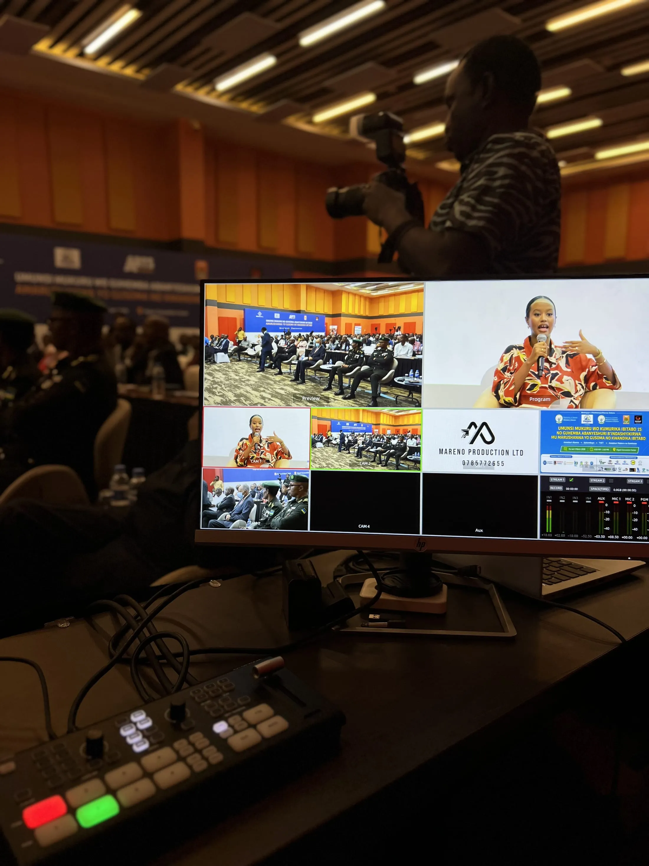 Photographer and broadcast monitor covering a national book launch and reading competition awards ceremony, with uniformed officials in attendance