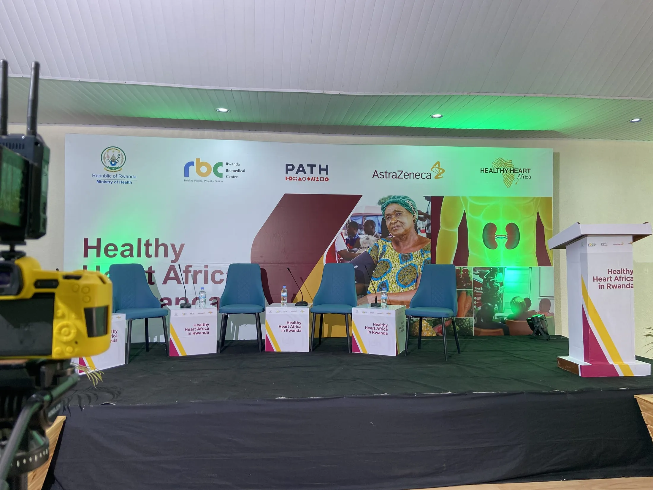 Camera operator covering a panel discussion at the Healthy Heart Africa forum, with RBC, PATH and AstraZeneca branding on stage